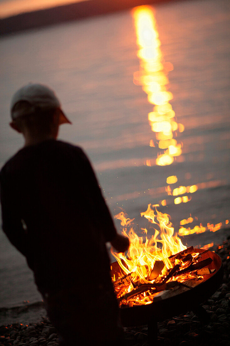 Junge am Lagerfeuer am Ufer des Starnberger Sees, Bayern, Deutschland