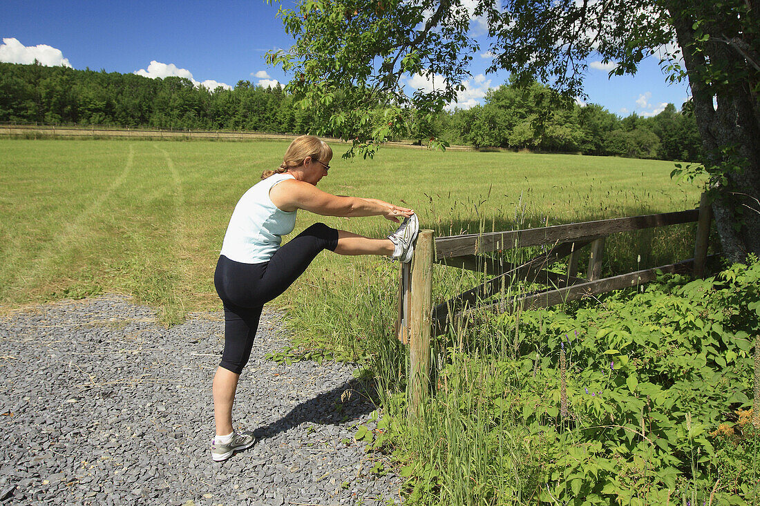 Jogger or runner stopping to stretch by a field and country road