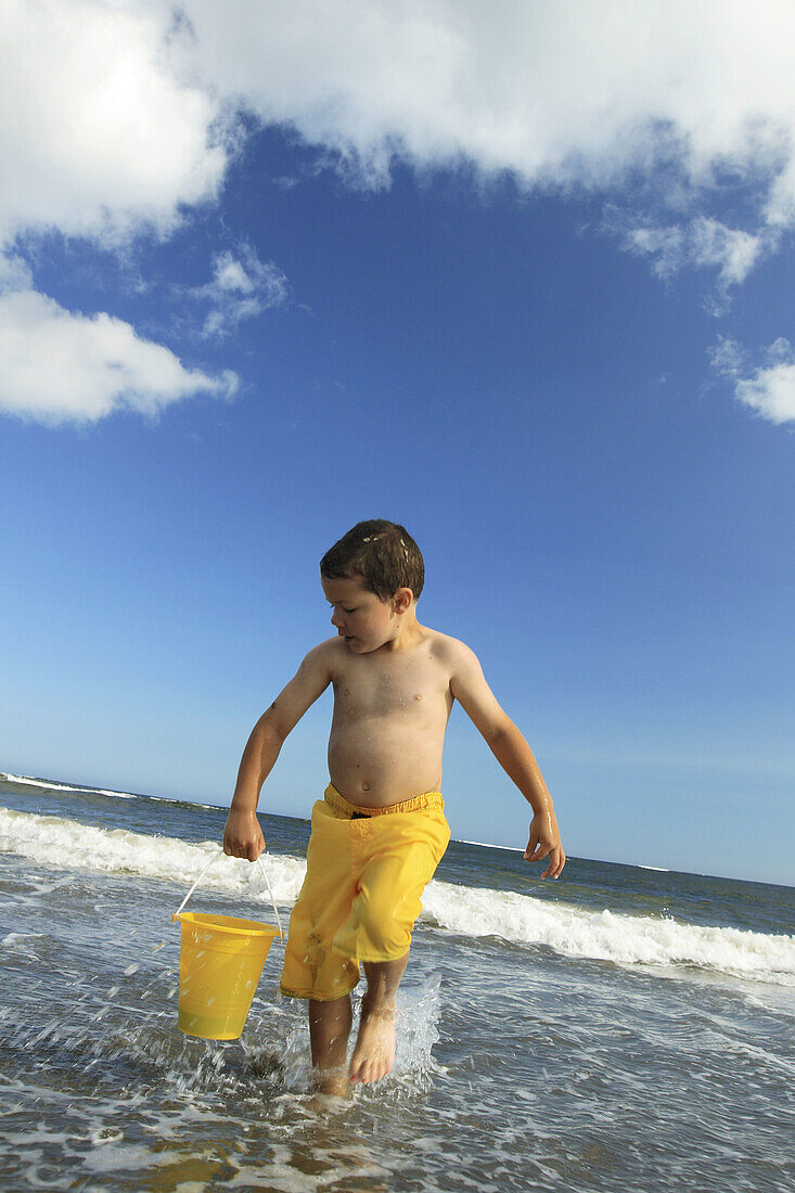 a 5 yr old boy carrying a pail of water at the beach
