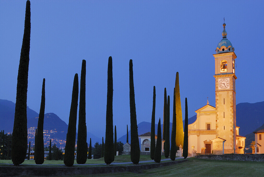 Illuminated church San Abbondino near Gentilino with cypress alley, Gentilino, Lugano, Ticino, Switzerland