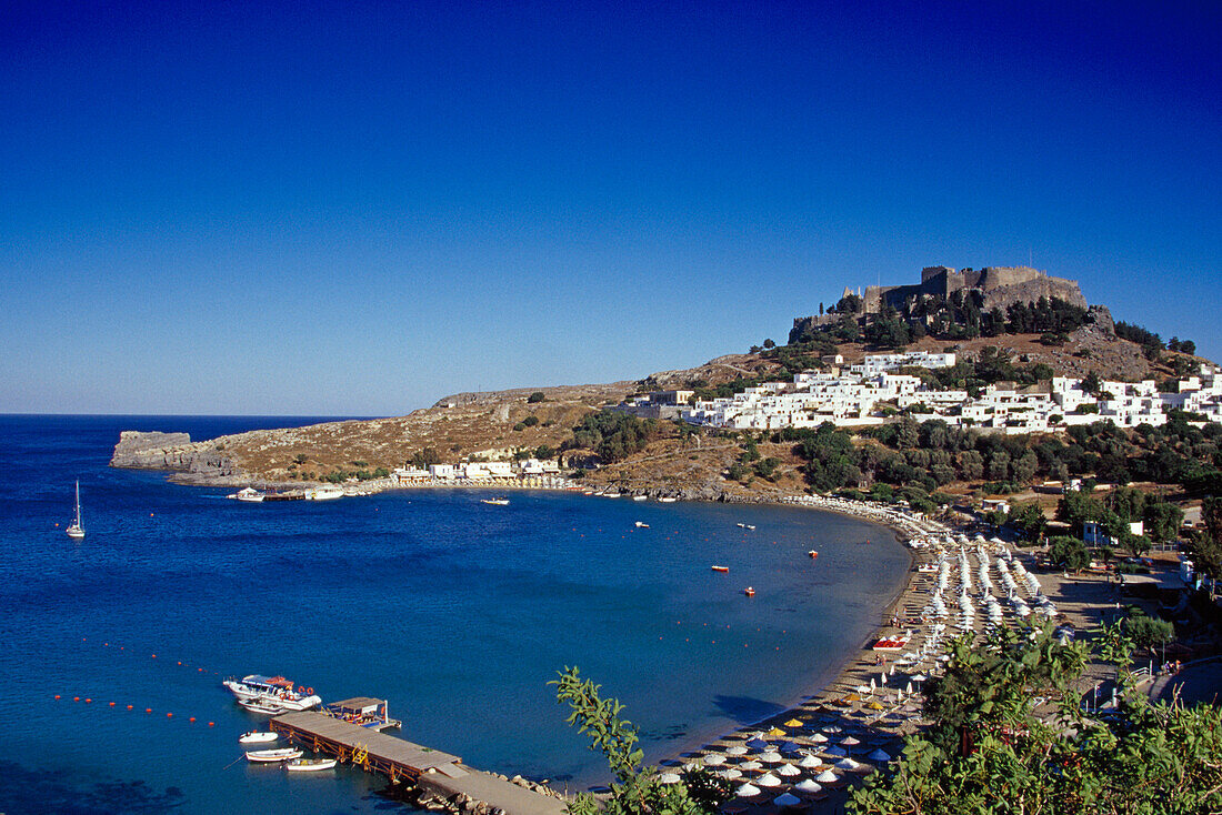 View at beach in a bay and acropolis under blue sky, Lindos, Island of Rhodes, Greece, Europe