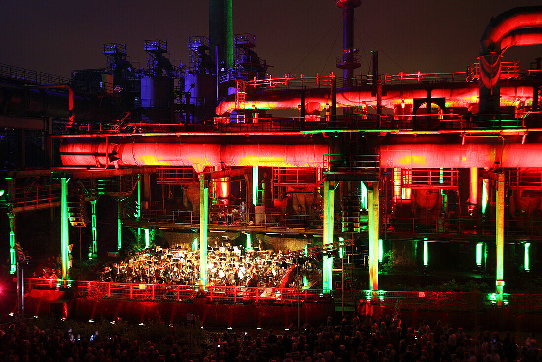 The Duisburg Philharmonic Orchestra playing in front of the illuminated backdrop of the Huette Meiderich, Duisburg, Ruhr Area, North Rhine-Westphalia, Germany, Europe