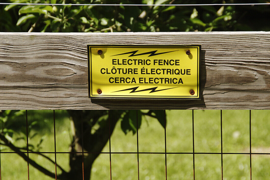 Electric fence sign on wood-and-wire fence, tree and grass behind, south central Indiana, USA