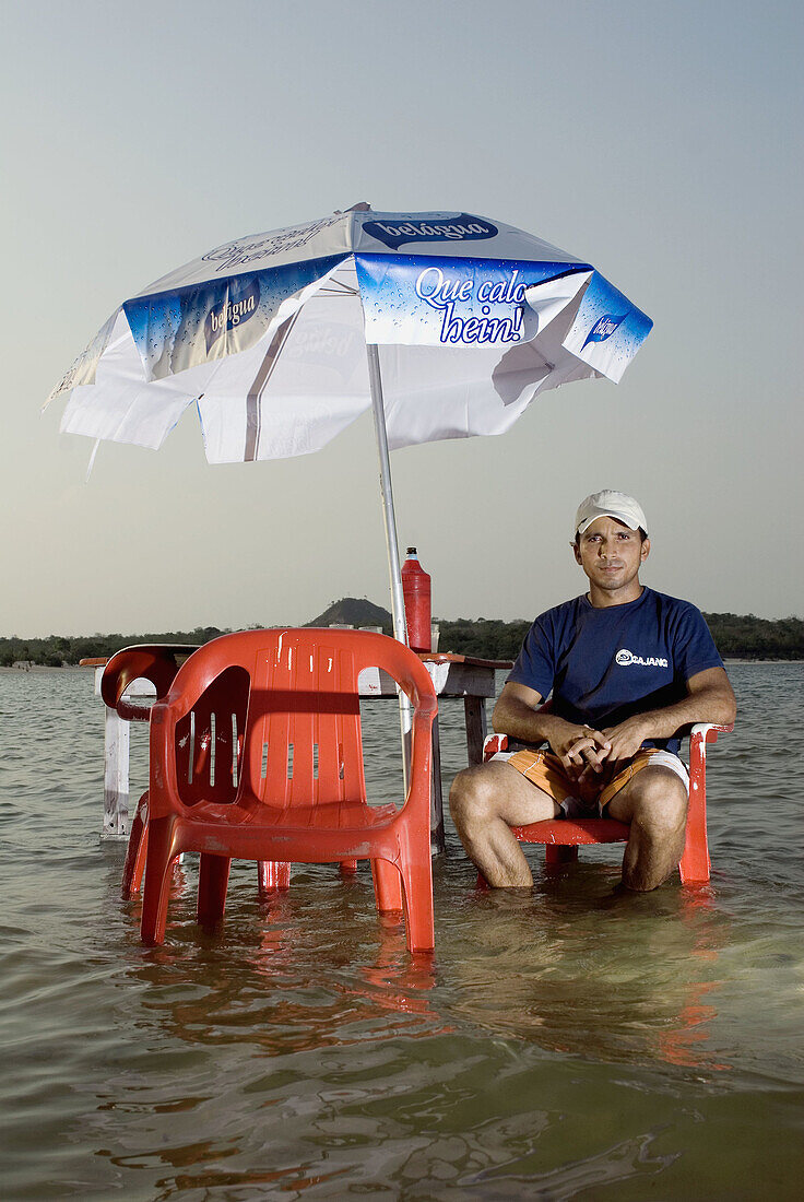 Elifler Leal, sitting in one of his bar tables on the beach, in Alter do Chão. Alter do Chão is surrounded by sweet water natural beaches, in Tapajós riverside, tributary of the Amazonas river. Brazil.