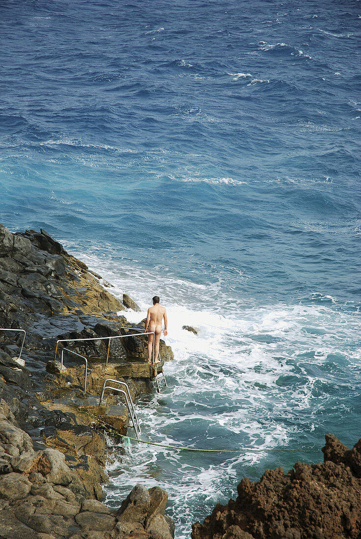 Nudist man on the rocks by the sea, natural pool in Charco del Palo, Lanzarote island, Canary Islands, Spain