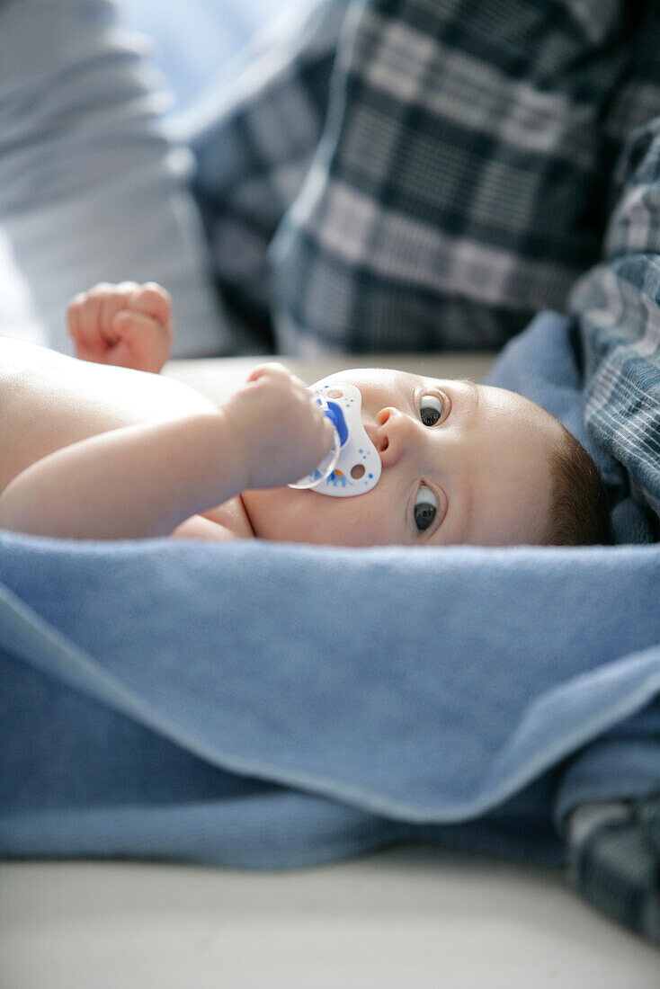 Baby (8 Monate) mit einem Schnuller liegt auf einer Decke, Wien, Österreich
