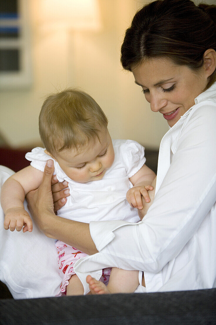 Mutter hält Baby (8 Monate) im Arm, berührt Brust, Wien, Österreich