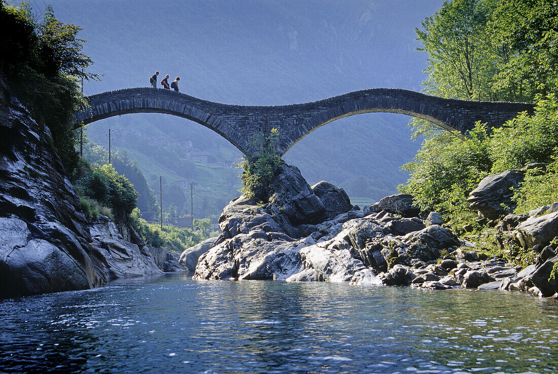 Hikers on the stone bridge Ponte dei Salti at Valle Verzasca, Ticino, Switzerland, Europe
