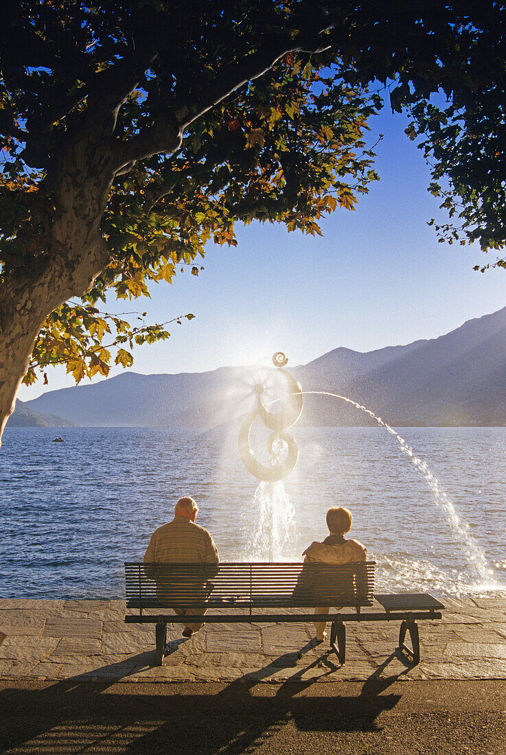 Man and woman sitting on a bench at the lakeside, Ascona, Lago Maggiore, Ticino, Switzerland, Europe