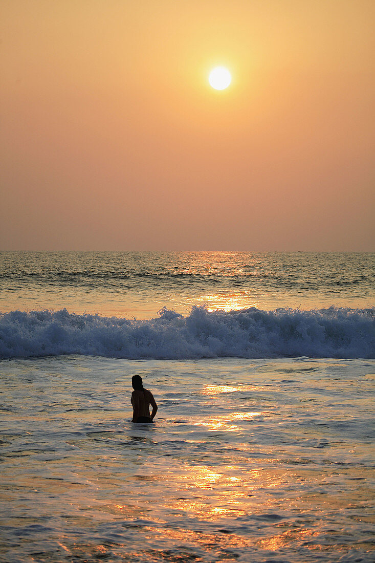 Bathing man at sunset, Lighthouse beach, Kerala, India