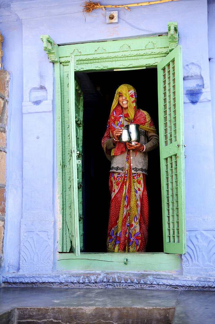 A colorful Rajasthani woman stands at the front door of her house, the house is a traditional colorful house