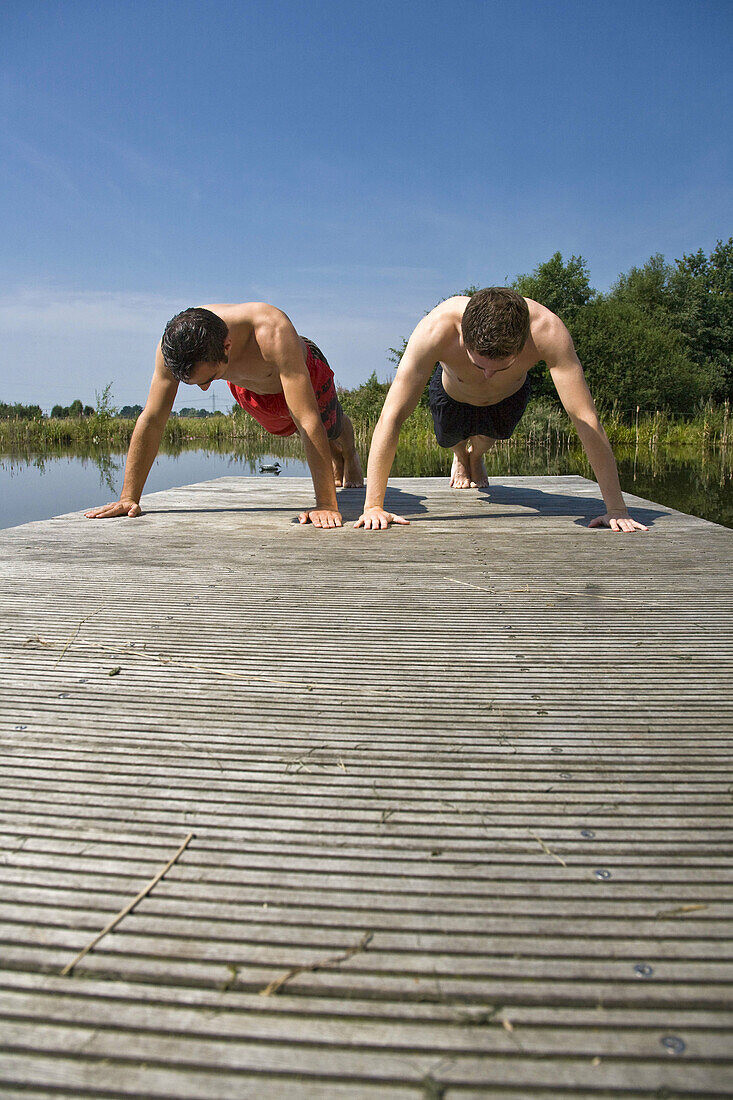 Two young men doing pushups on a plank