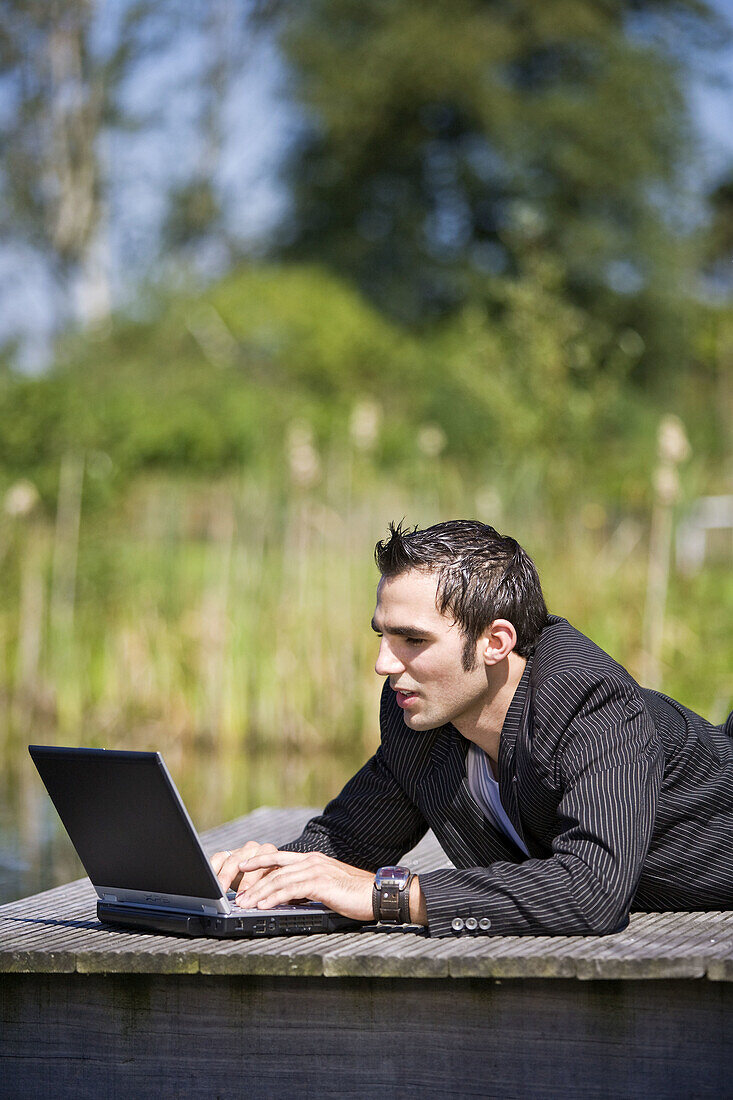 Young man lying on a plank working on his laptop computer