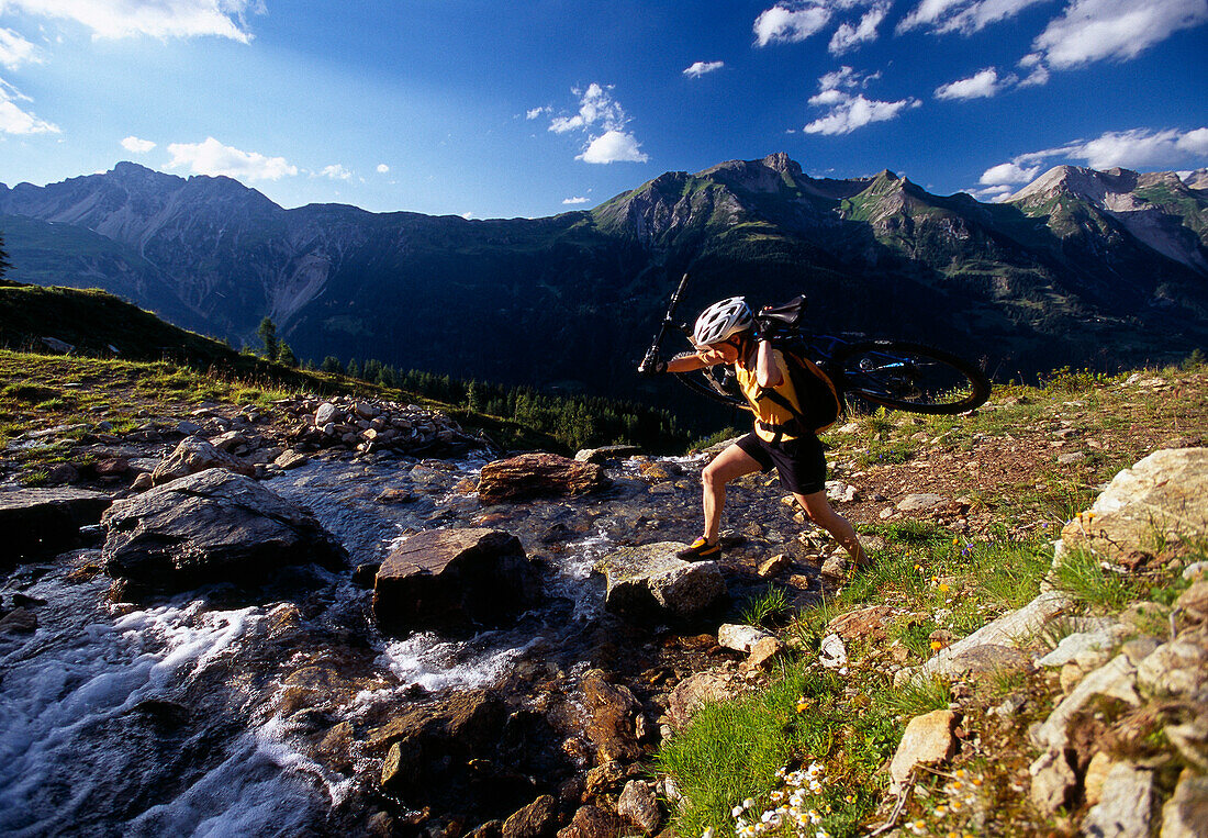 A woman carrying her mountain bike across a mountain stream, Tyrol, Austria, Europe