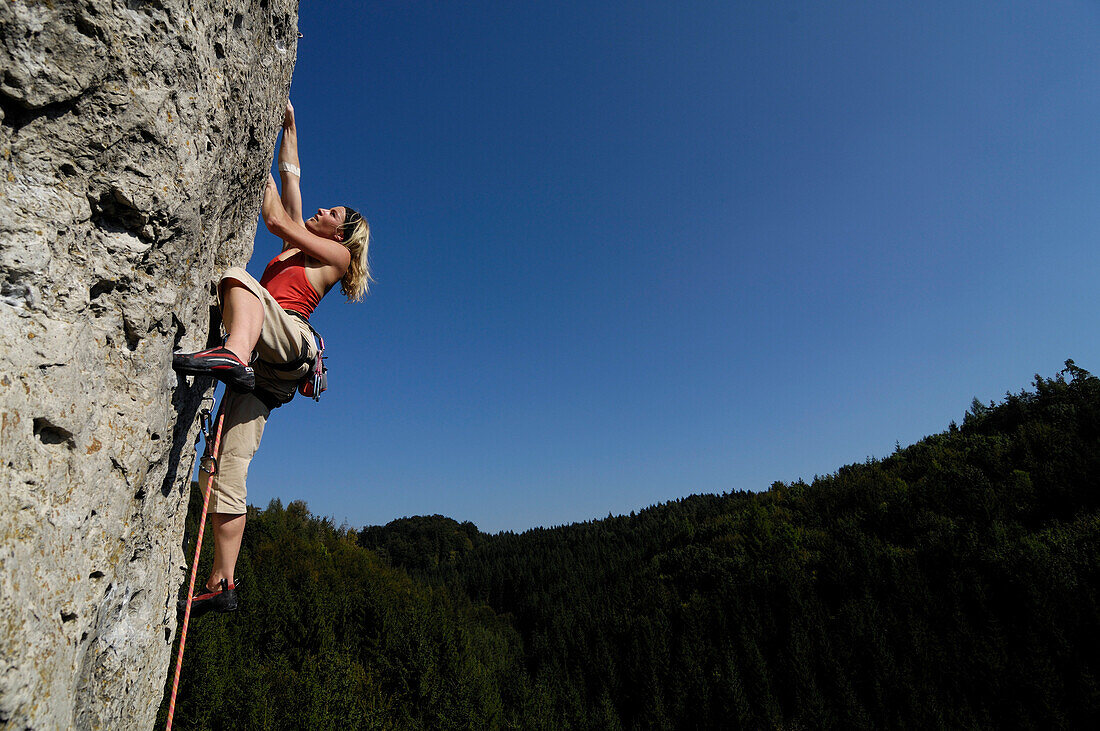 Frau klettert an einer Felswand im Sonnenlicht, Fränkische Schweiz, Bayern, Deutschland, Europa