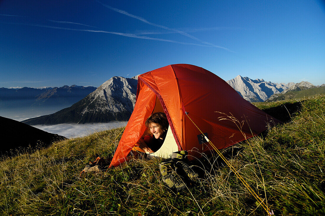 Young woman looking out of a tent in the mountains, Tyrol, Austria, Europe