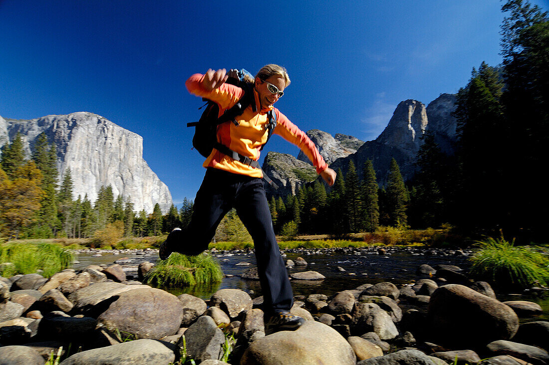 Frau mit Rucksack springt über Steine am Bachufer, Yosemite Nationalpark, Kalifornien, Nordamerika, Amerika