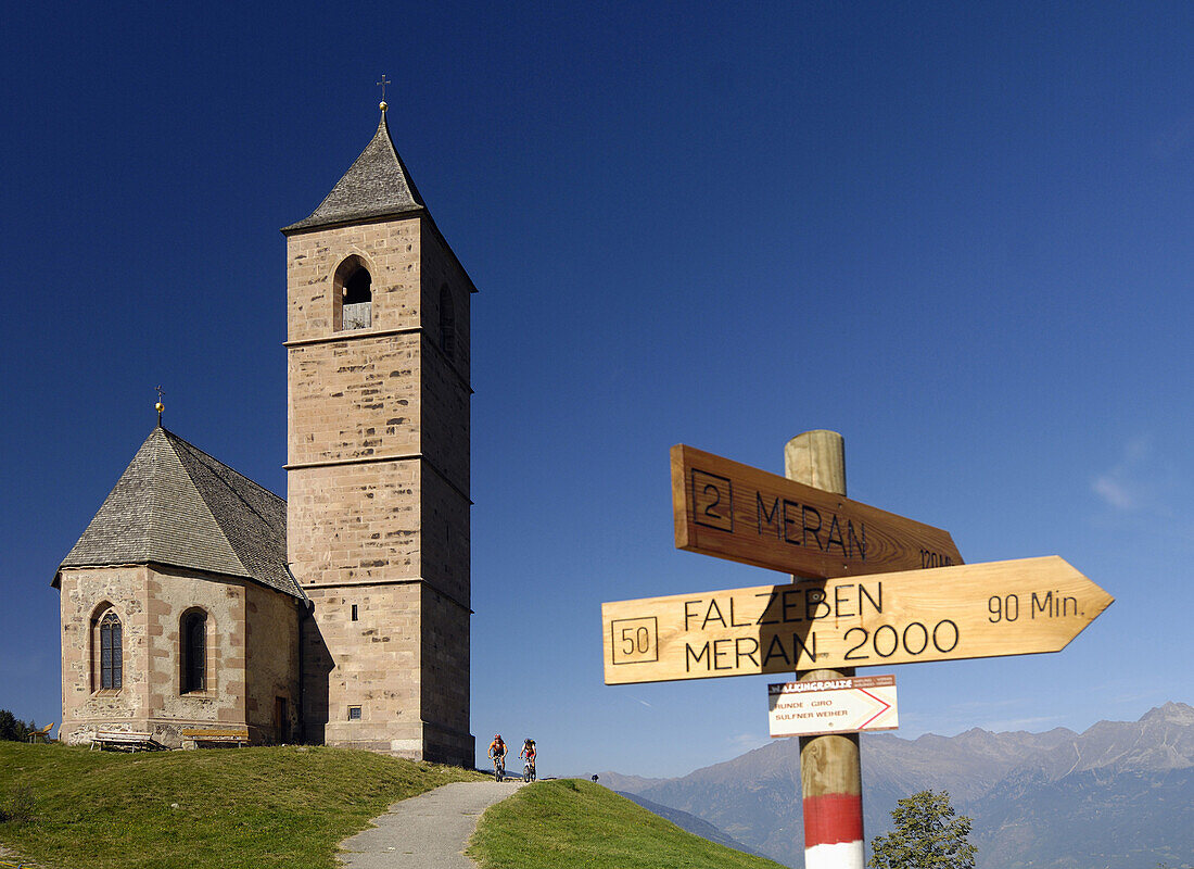Two mountain bikers near Sankt Kathrein church, Hafling, Trentino-Alto Adige/Südtirol, Italy