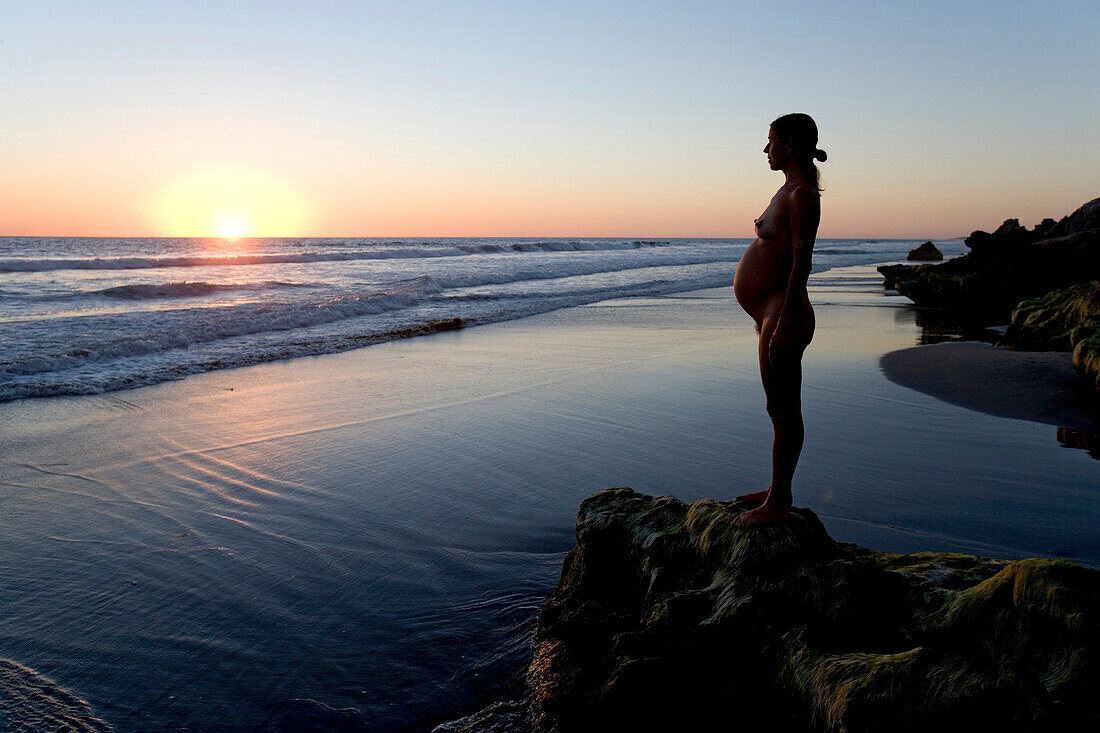 Pregnant woman standing on a rock on the beach at sunset, Conejo beach, Baja California Sur, Mexico