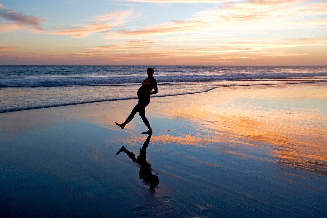Schwangere Frau geht über den Strand und hält sich den Bauch, Sonnenuntergang, Strand von Conejo, Baja California Süd, Mexiko