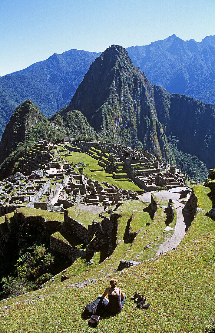 Machu Picchu Inca ruins, terraces, visitor sitting on terrace, and Huayna Picchu, Peru