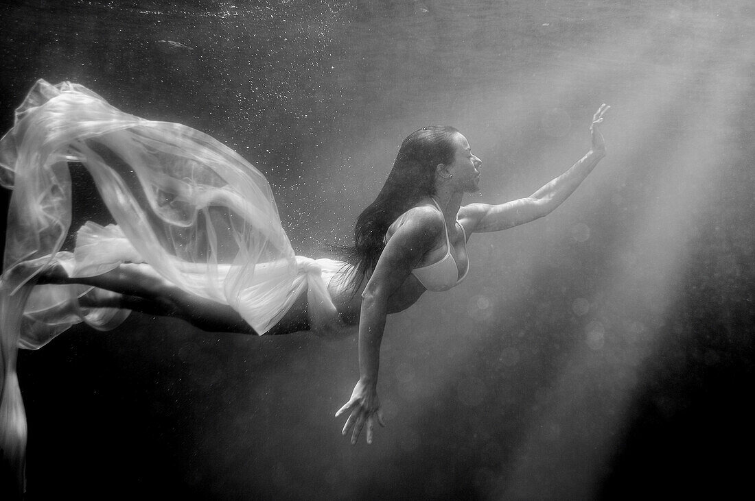 Girl swimming underwater, searching for the light