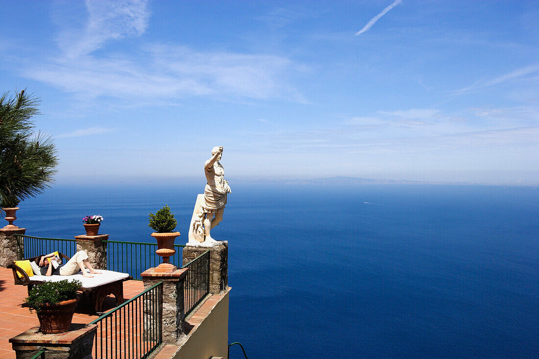 Eine Frau liegt lesend auf einer Terrasse mit Meerblick, Capri, Italien, Europa