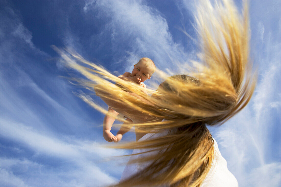 A woman with hair flying holds her 5 month old baby in the air, Nine Palms, Baja California Sur, Mexico