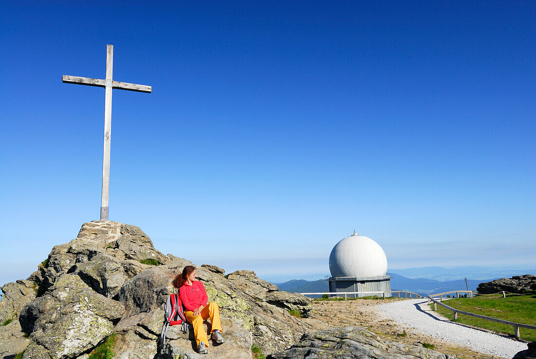 Frau sitzt unter einem Gipfelkreuz, Großer Arber, Nationalpark Bayerischer Wald, Niederbayern, Bayern, Deutschland