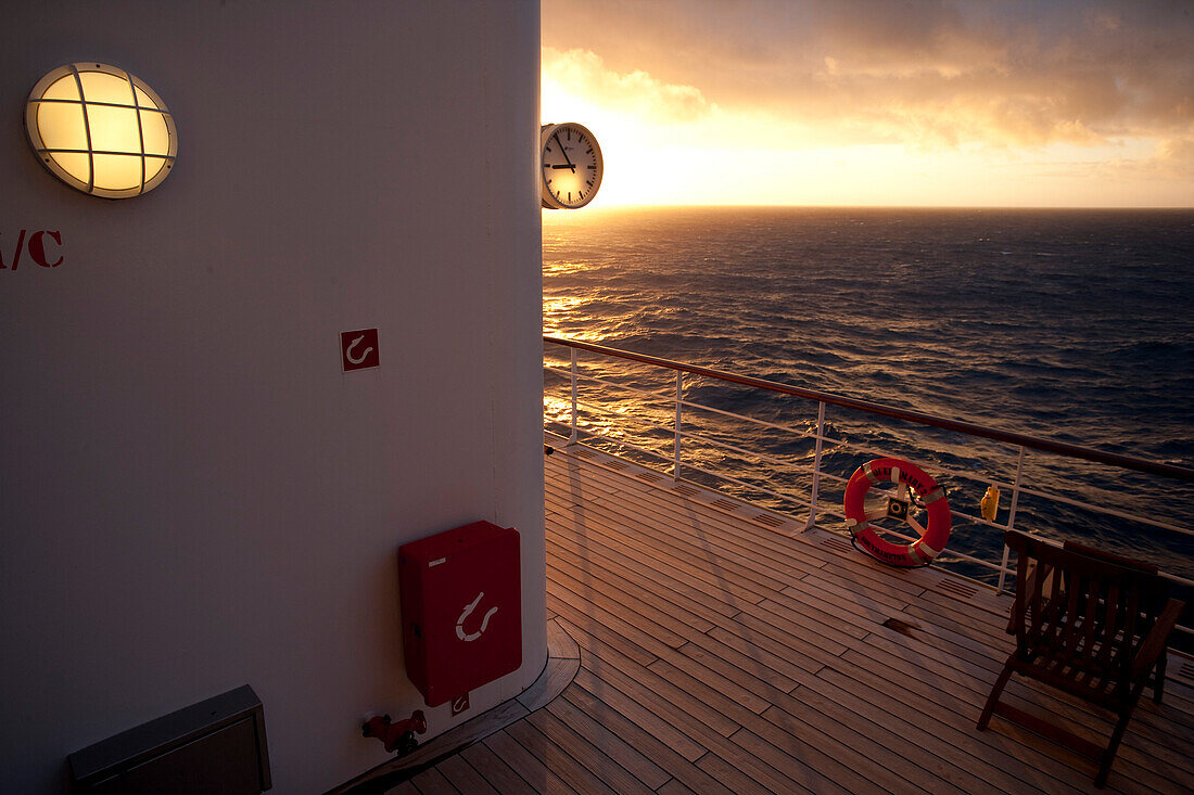 Promenadendeck mit Uhr, Rettungsring und Liegestuhl, Sonnenuntergang, Kreuzfahrtschiff Queen Mary 2, Transatlantik, Nordatlantik, Atlantik