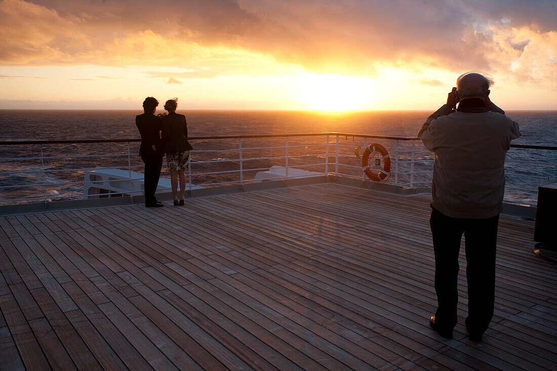 Junges Paar schaut sich den Sonnenuntergang an, Passagiere auf dem Achterdeck, Kreuzfahrtschiff Queen Mary 2, Transatlantik, Nordatlantik, Atlantik