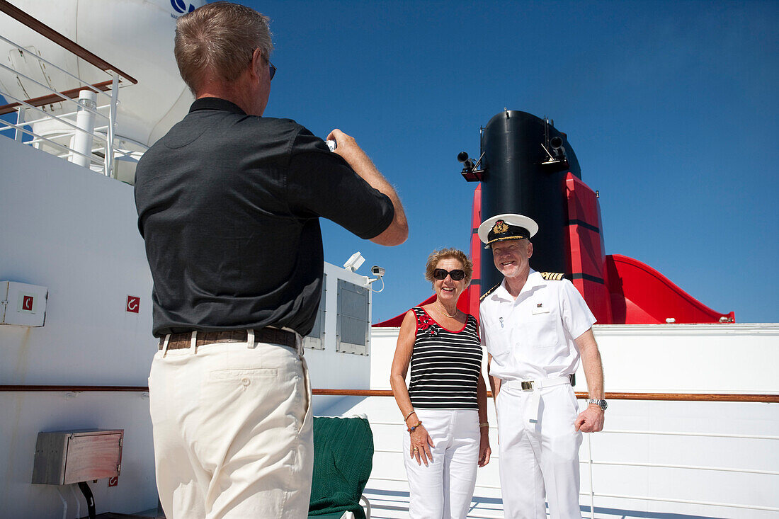 Kapitän Christopher Rynd posiert mit Gästen, Sonnendeck, Kreuzfahrtschiff Queen Mary 2