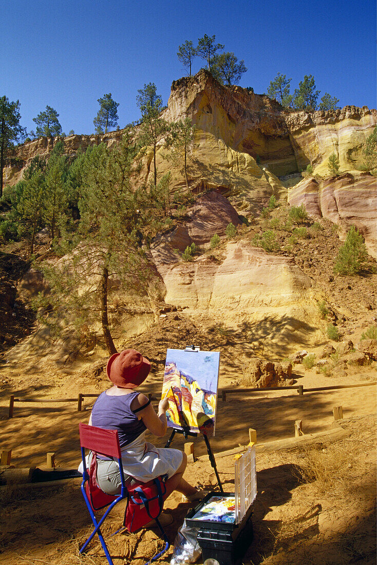Paintress with easel at the ochre rocks at Val de Fées under blue sky, Vaucluse, Provence, France, Europe