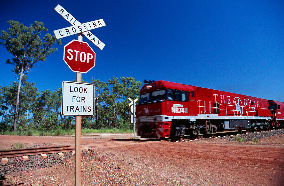 Red engine of The Ghan train near level crossing sign, Darwin, Northern Territory, Australia
