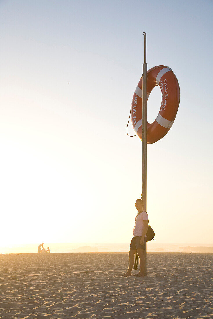 Mann am Strand bei Sonnenuntergang, rettungsring auf Pfahl, Abendlicht, Atlantik, beliebter Strand von Windsurfern, Praia de Odeceixe, Algarve, Portugal