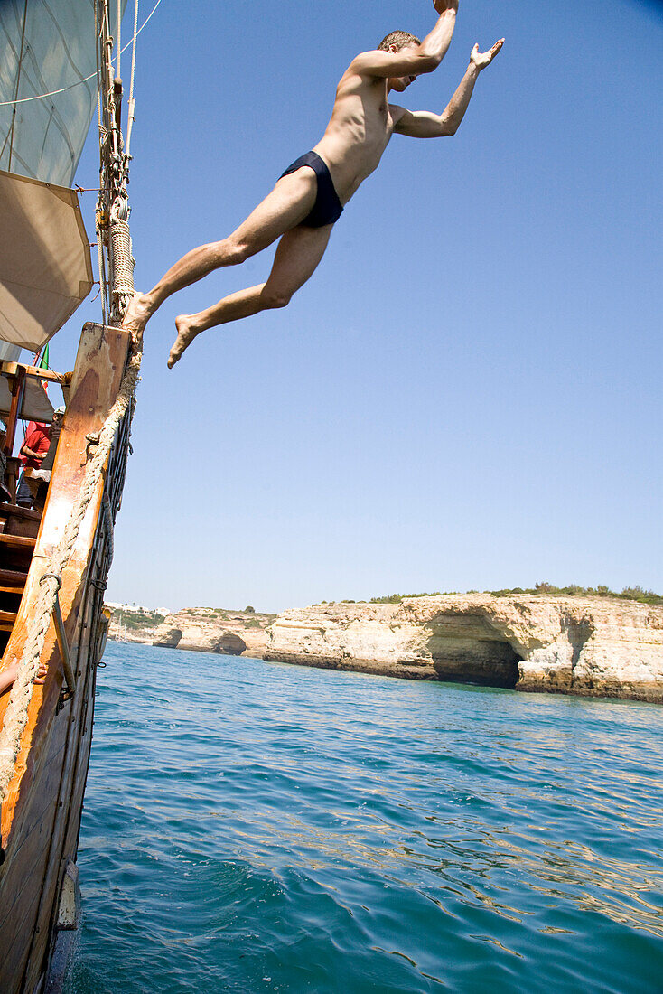 Junger Mann springt vom Segelschiff Santa Bernada ins Wasser, fuer touristische Zwecke umgebautes altes Segelschiff, Fahrten entlang der Felsenkueste, MR, Portimao, Algarve, Portugal