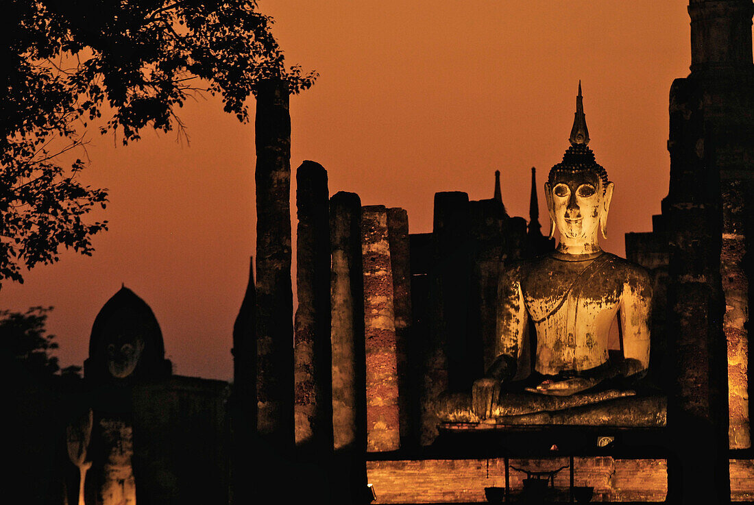 Illuminated Buddha in the evening light with orange coloured sky at Wat Mahathat, Sukothai Historical Park, Central Thailand, Asia