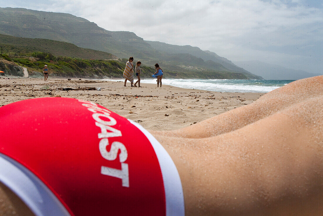 Man with red swimming trunks on the beach under clouded sky, Bosa, Sardinien, Europe