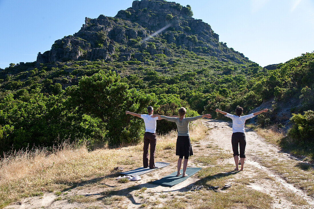 Drei Personen machen Yoga vor einem Berg im Licht der Morgensonne, Jerzu, Sardinien, Italien, Europa