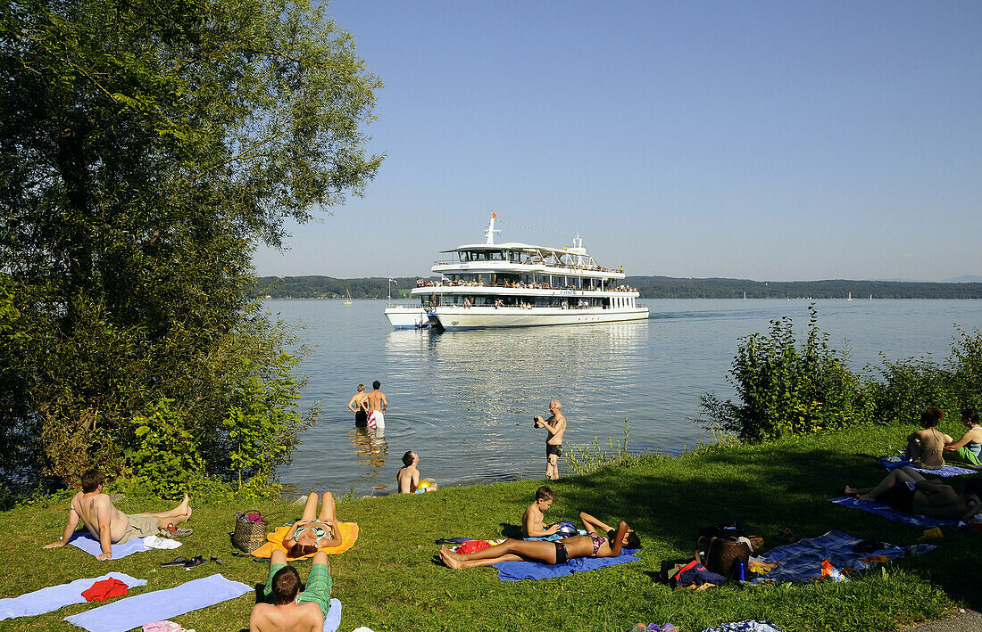 People sunbathing at lake Starnberg, pleasure boat in background, Bernried, Bavaria, Germany
