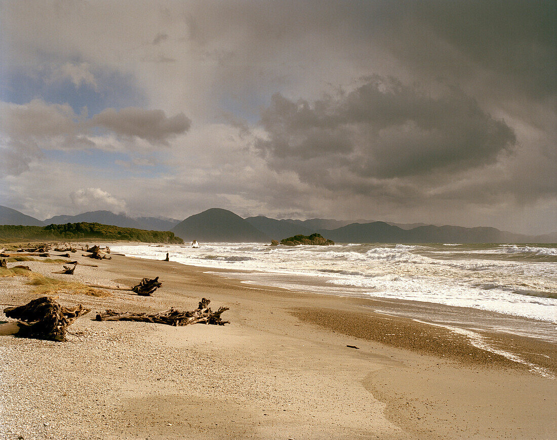 Strand mit Treibholz und Brandung unter grauen Wolken, Okuru Beach, Westküste, Südinsel, Neuseeland