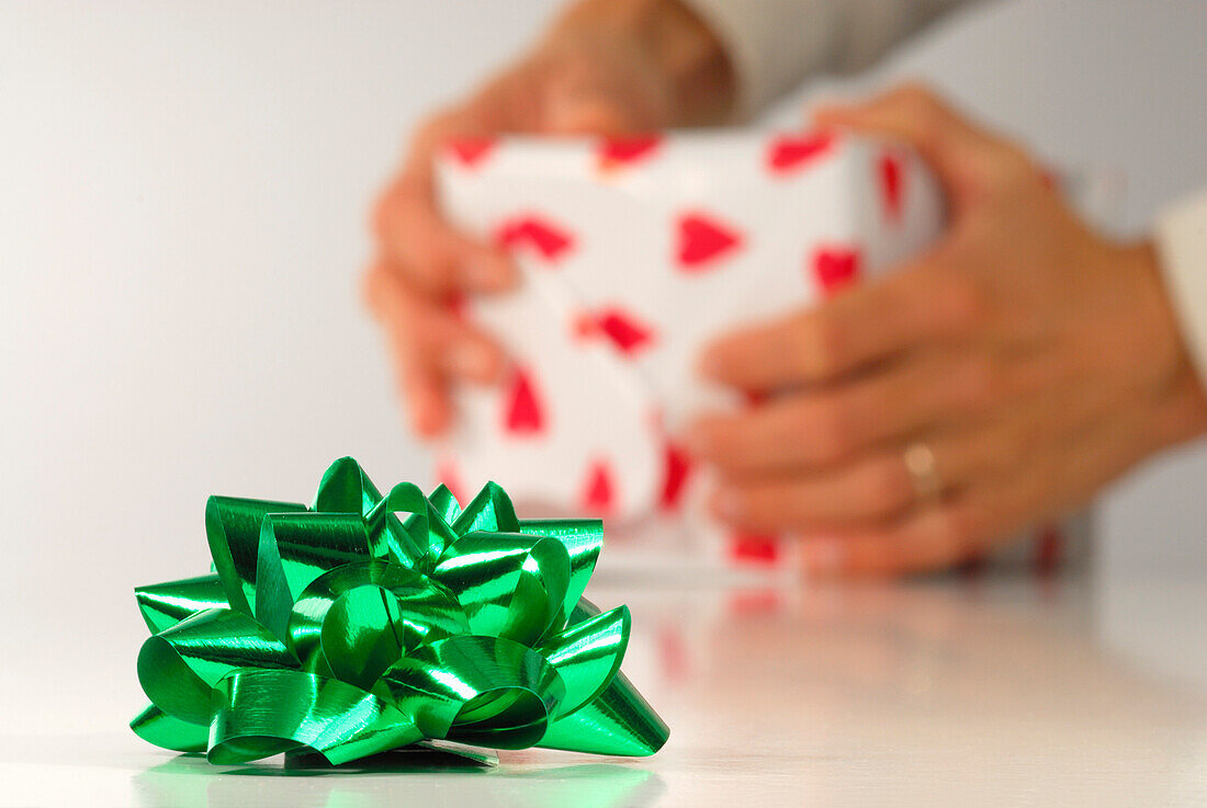 Grüne Geschenkschleife mit Person im Hintergrund, die Geschenk einpackt