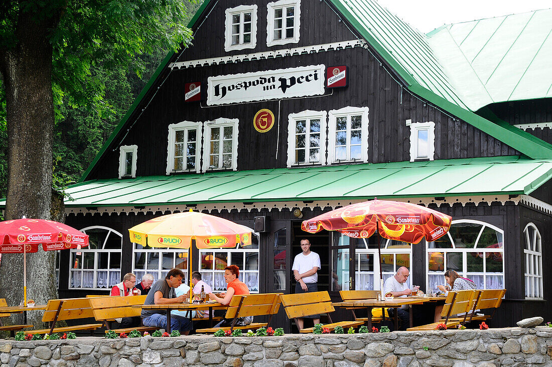 Menschen sitzen vor dem Gasthaus na Pezi im Dorf Pec, Riesengebirge, Ost-Böhmen, Tschechien, Europa