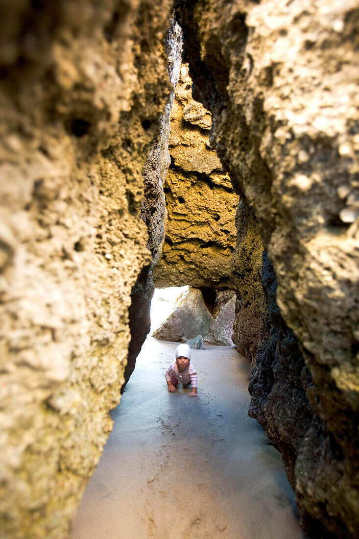 Ein kleines Mädchen krabbelt am Strand durch eine Höhle, Punta Conejo, Baja California Sur, Mexiko, Amerika