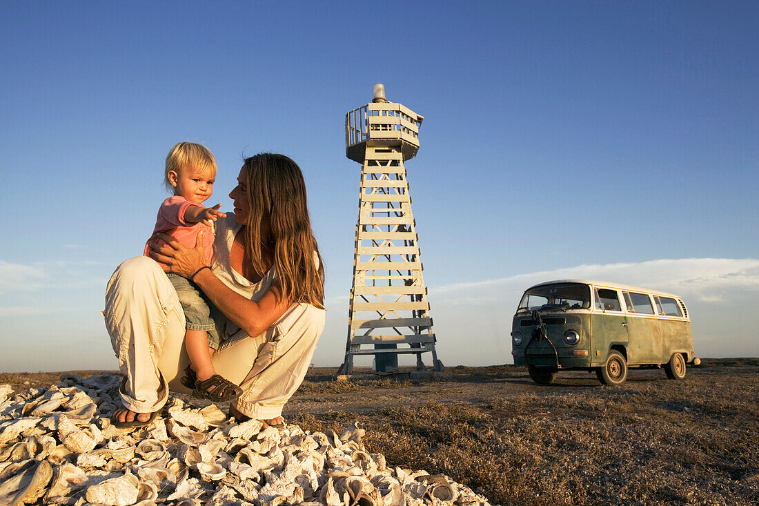 A woman with child sitting in front of a lighthouse in the sunlight, Punta Conejo, Baja California Sur, Mexico, America