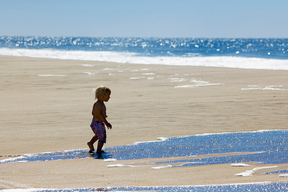 Kleines Mädchen geht über den Sandstrand zum Meer, Punta Conejo, Baja California Sur, Mexiko, Amerika