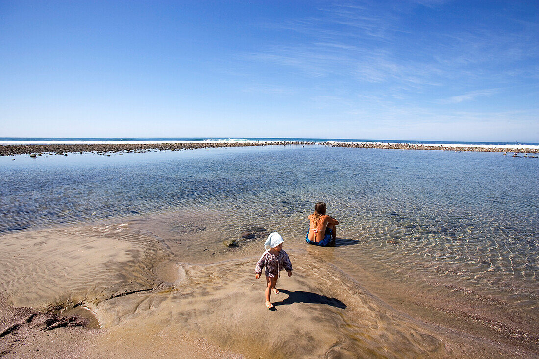 Blick auf eine Frau und ein Kind an einer kleinen Lagune im Sonnenlicht, Punta Conejo, Baja California Sur, Mexiko, Amerika