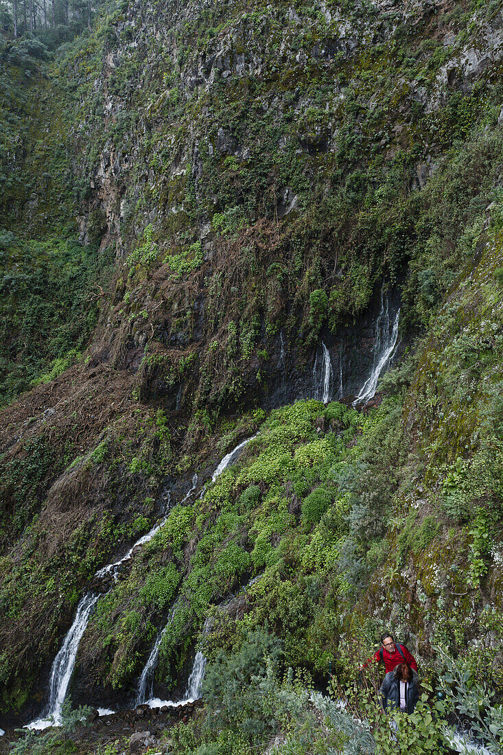 Couple hiking near the waterfall, Galeria de agua, Fuente Marcos, Fuentes Marcos y Cordero, natural preserve, Parque Natural de las Nieves, east side of extinct volcanic crater, Caldera de Taburiente, above San Andres, UNESCO Biosphere Reserve, La Palma, 