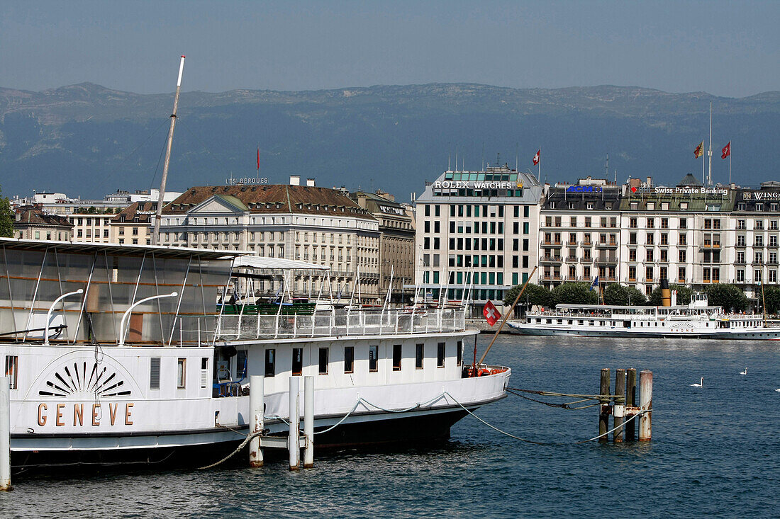 Cruise Boat On Lake Geneva In Front Of The City'S Typical Buildings On The Harbour Of Geneva, Switzerland