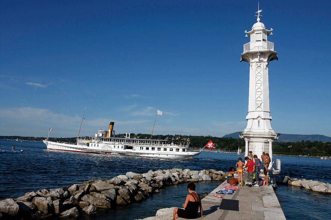 Cruise Boat And Relaxing Around The White Lighthouse Of The Bains Des Paquis In The Geneva Harbour On Lake Geneva, Geneva, Switzerland